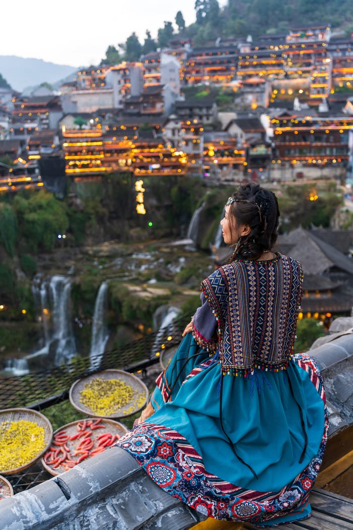 Mujer en traje típico viendo la ciudad de Lijiand China al anochecer
